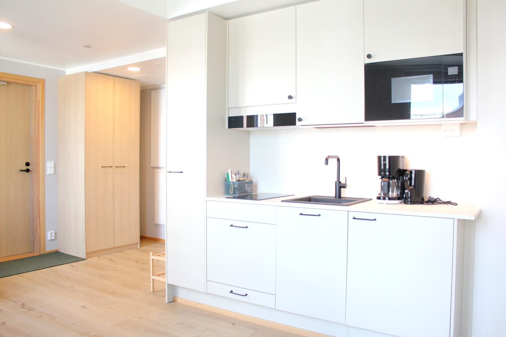 Bright, modern kitchen with white cabinets, built-in oven, and coffee station along a white counter under bright lighting